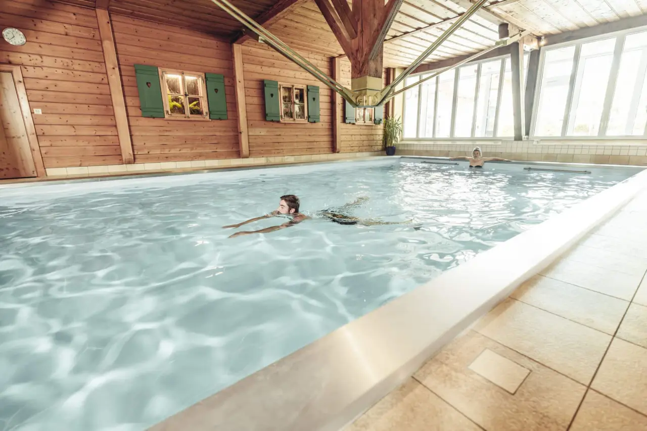 Innenpool mit rustikalem Holzambiente und schwimmenden Gästen im Wellness- und Vitalhotel Böhmhof.
