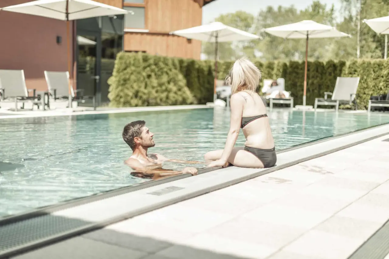 Paar entspannt am Aussenpool des Böhmhof - Wellness- und Vitalhotel unter Sonnenschirmen und grüner Hecke.