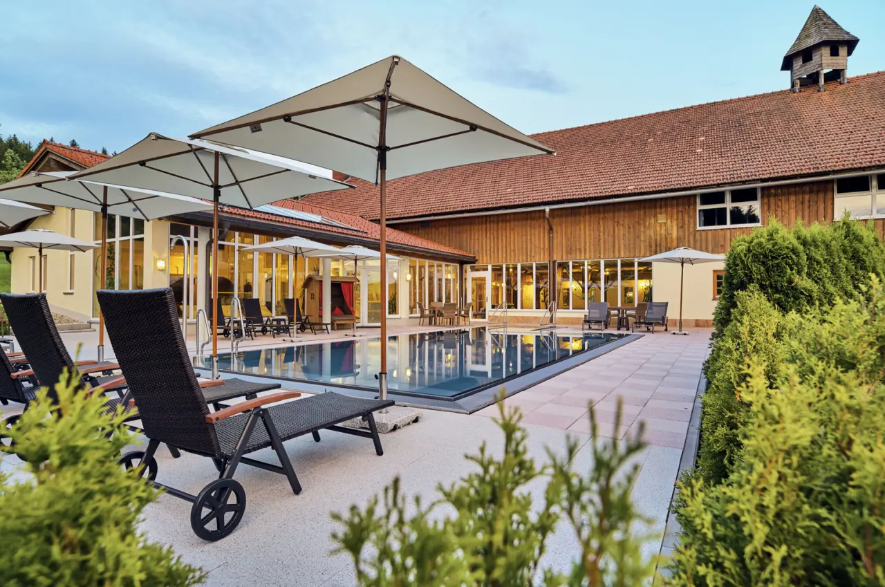 Abendliche Aussenansicht des Pools mit Liegestühlen und Hotelgebäude im Wellness- und Vitalhotel Böhmhof.