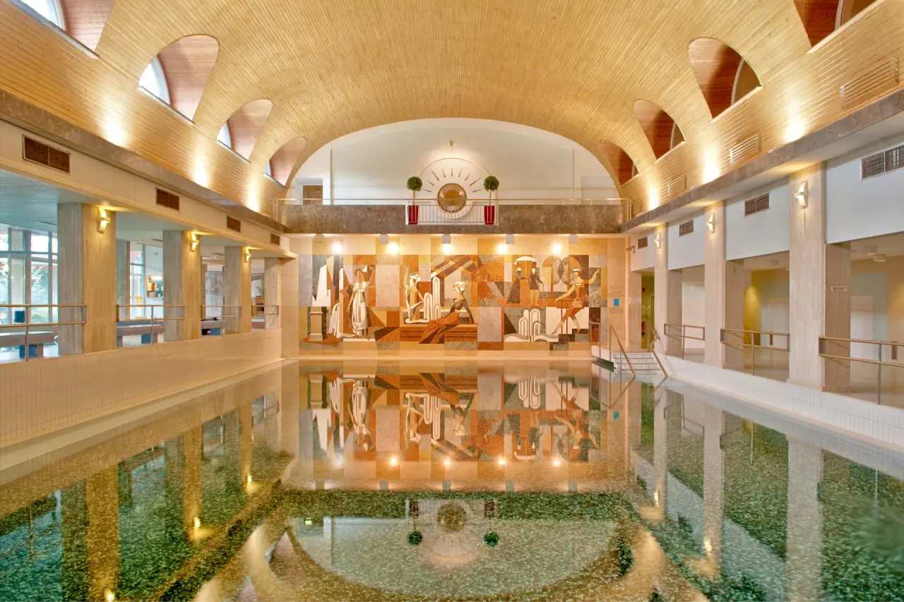 Grosszügiger Innenpool mit Holzbogendecke und kunstvollem Wandmosaik im Thermenhotel Karawankenhof.