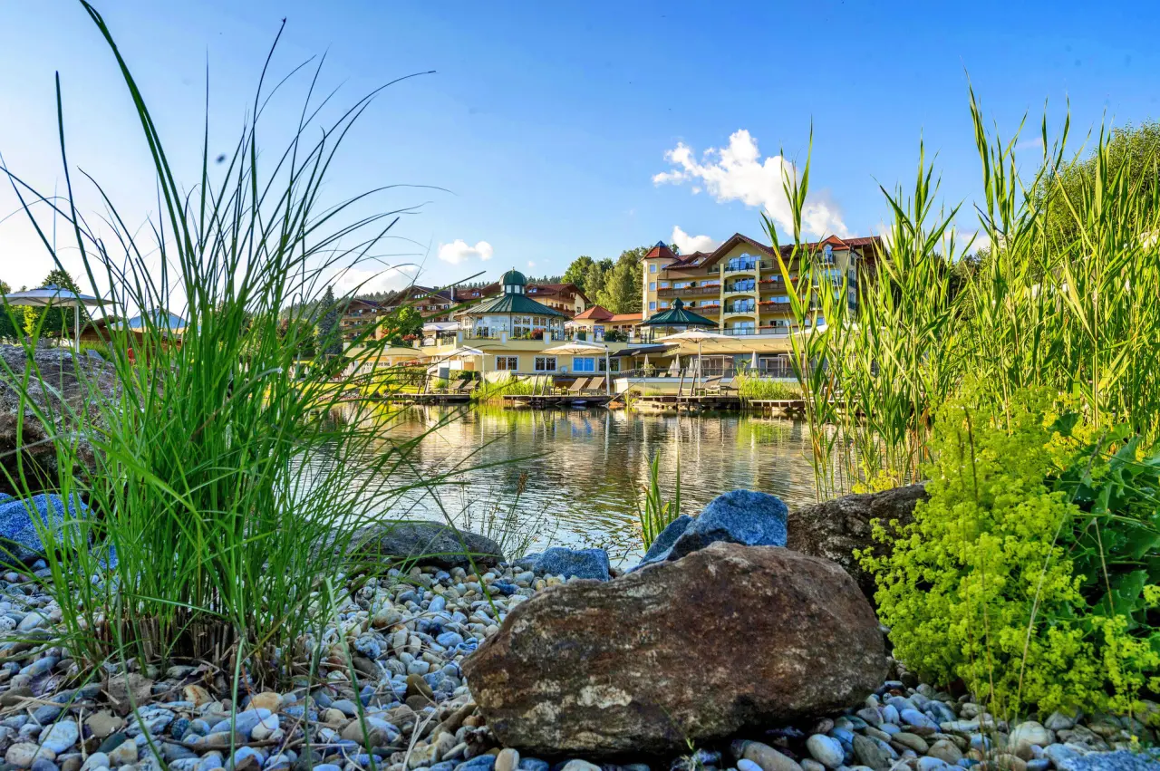 Wellness & SPA Resort Mooshof mit Natur-Badeteich und Liegedecks unter blauem Himmel.