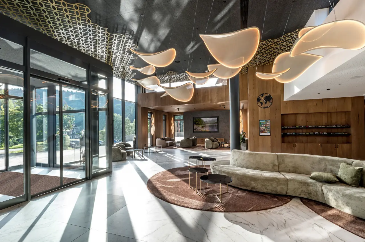 Moderne, lichtdurchflutete Lobby des Wellness & SPA Resort Mooshof mit stilvollen Designleuchten und Sitzbereichen.