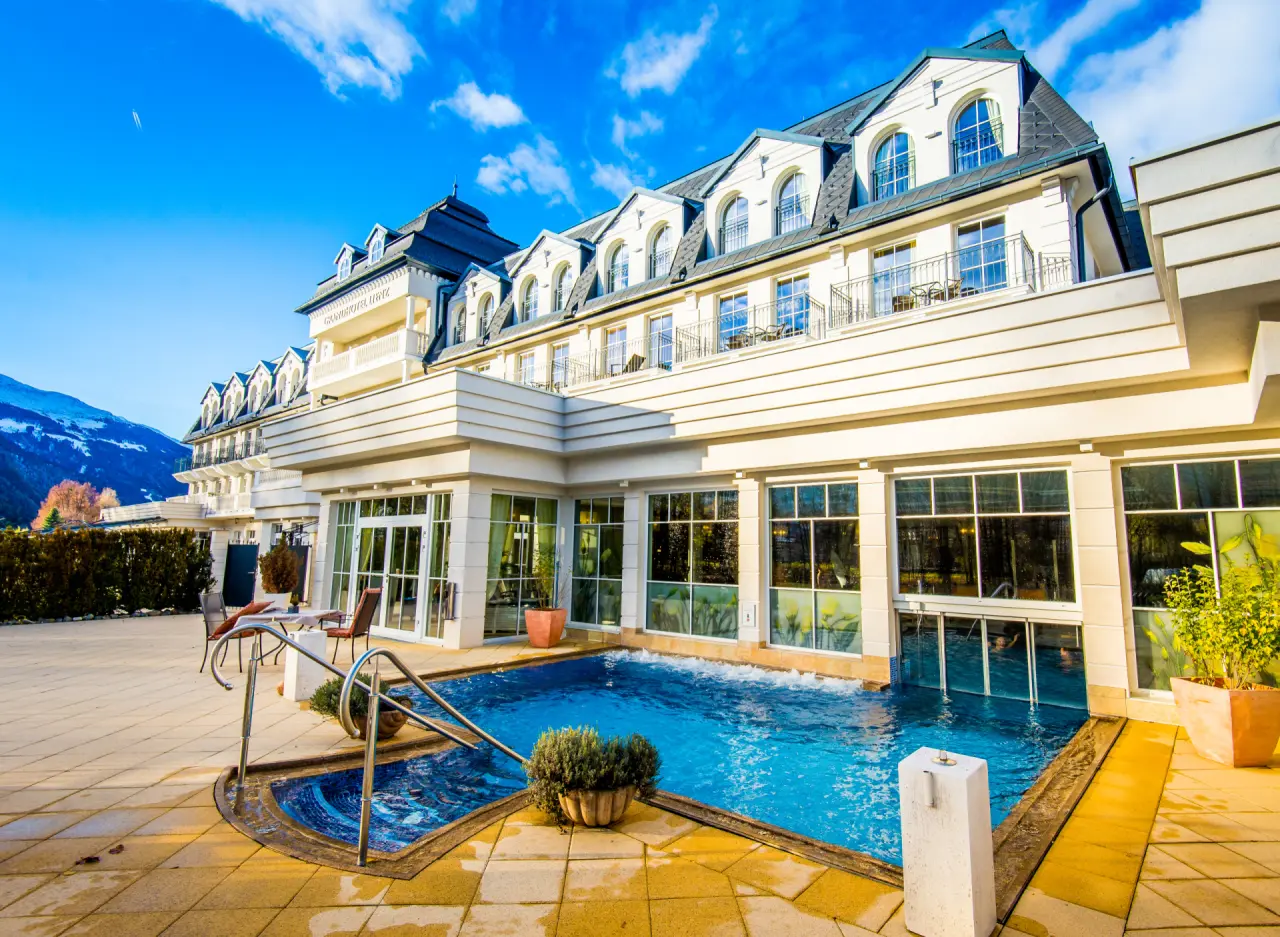 Aussenansicht des luxuriösen Grandhotel Lienz mit sonnigem Aussenpool und Bergblick unter blauem Himmel.