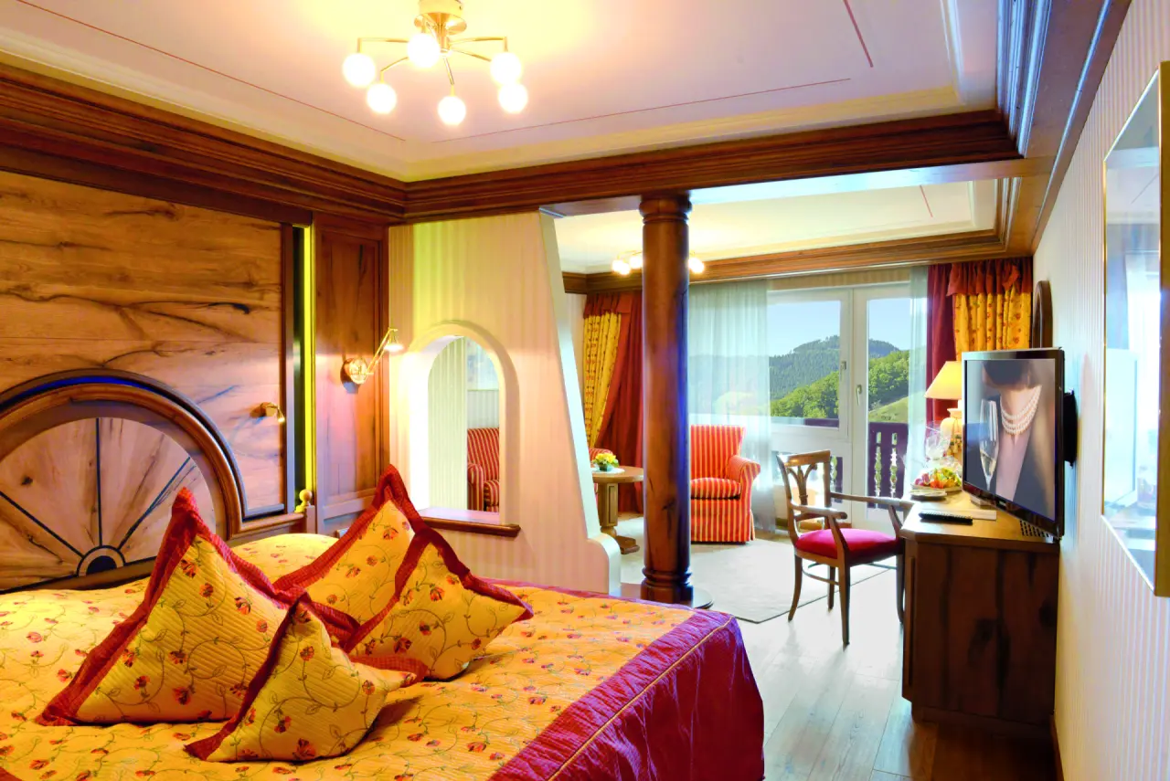 Gemütliches Hotelzimmer im Haus Dollenberg mit Doppelbett, Sitzbereich und Balkonblick auf die Berge.