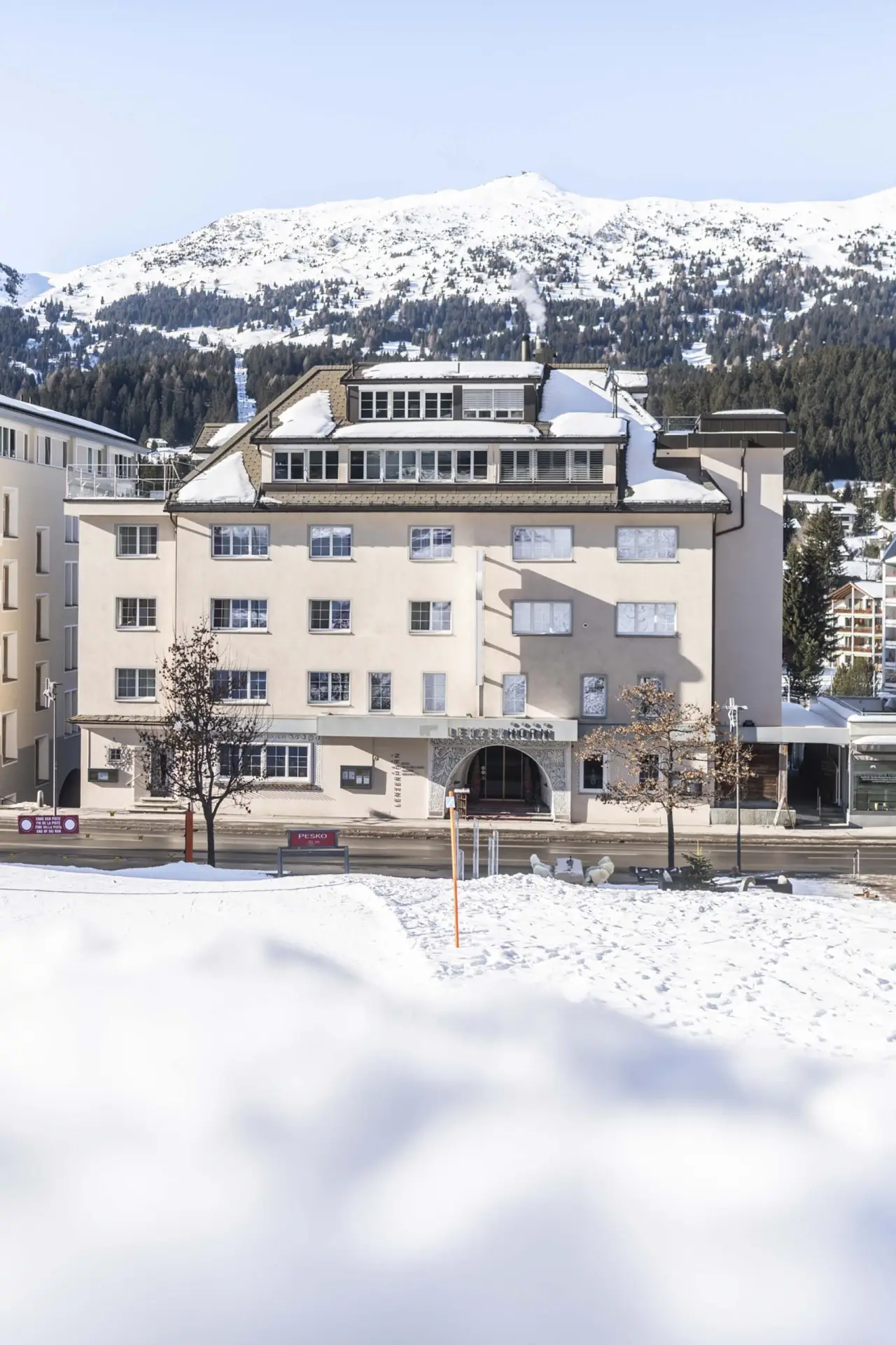 Aussenansicht des HOTEL LENZERHORN im Winter mit schneebedeckten Bergen im Hintergrund.