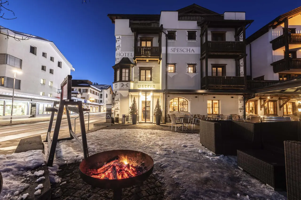 Winterliche Abendansicht des Hotel Lenzerhorn mit beleuchteter Fassade, Schnee und gemütlicher Feuerschale.