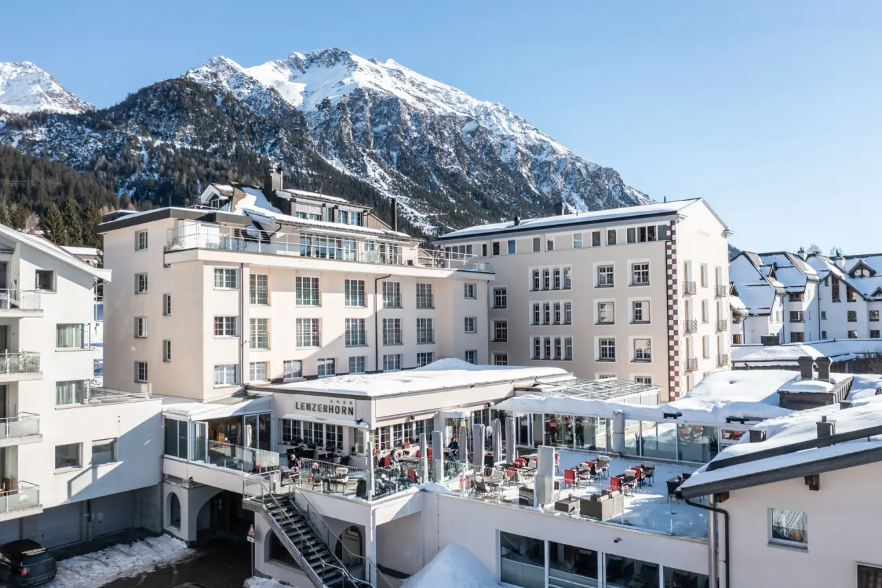 Aussenansicht des Hotel Lenzerhorn im Winter mit schneebedeckten Bergen im Hintergrund und sonniger Terrasse.