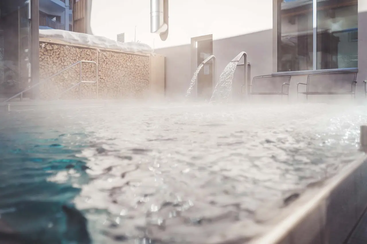 Beheizter Aussenpool mit sprudelnden Wasserfällen und Holzstapel im Schnee im Hotel LENZERHORN.