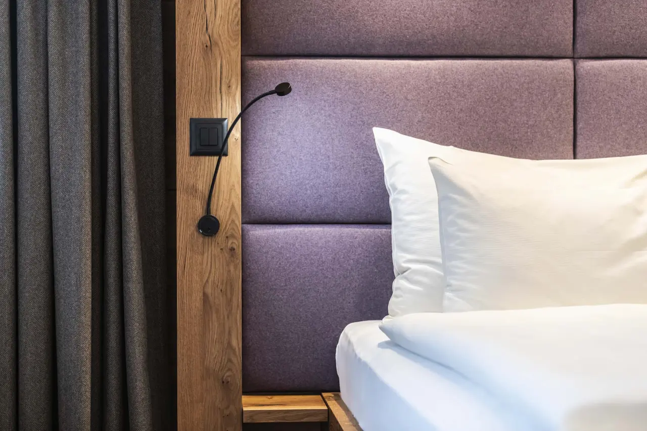 Modernes Hotelzimmer im HOTEL LENZERHORN mit lila Kopfteil, Holzelementen und Leselampe für entspannte Nächte.