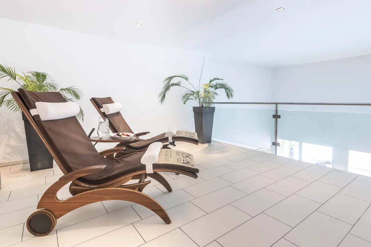 Heller Ruheraum mit eleganten Holz-Liegestühlen und Pflanzen im Wellnessbereich des Hotel Lenzerhorn.