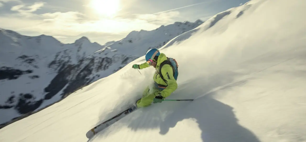 Dynamischer Skifahrer im Tiefschnee vor winterlicher Bergkulisse am Aktiv- & Wellnesshotel Pirchnerhof.
