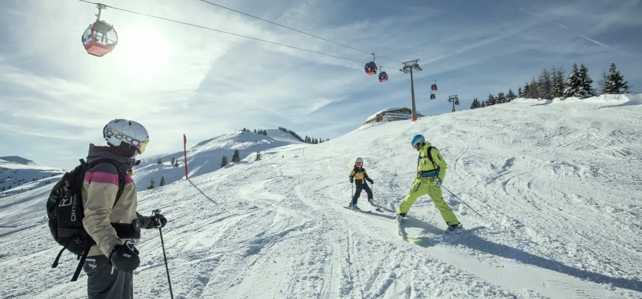 Skifahrer auf sonniger Piste mit Gondelbahn und Bergpanorama, nahe dem Aktiv- & Wellnesshotel Pirchnerhof.