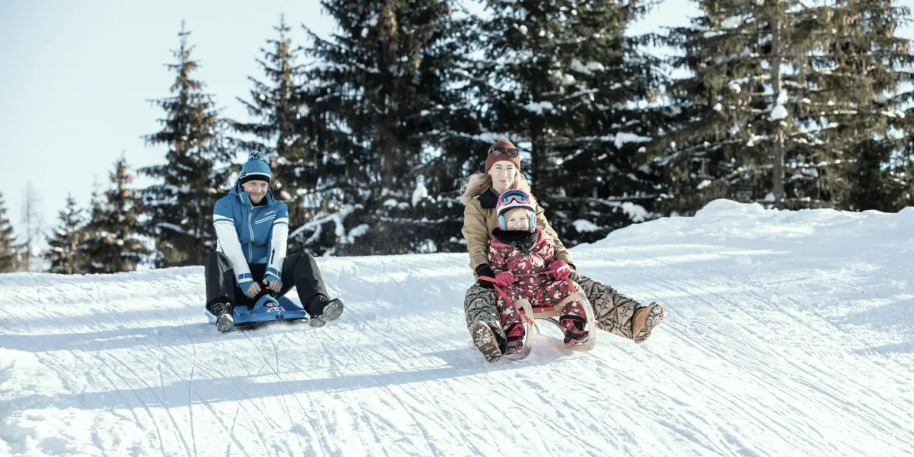 Familie rodeln im Schnee am Aktiv- & Wellnesshotel Pirchnerhof. Winteraktivität für Familienurlaub in den Bergen.