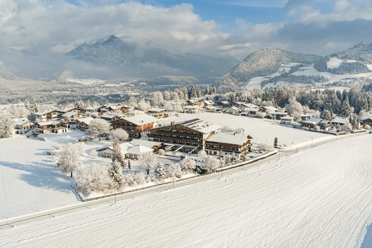 Winterliche Luftaufnahme des Aktiv- & Wellnesshotel Pirchnerhof, eingebettet in verschneite Alpenlandschaft mit Bergen und Dorf.