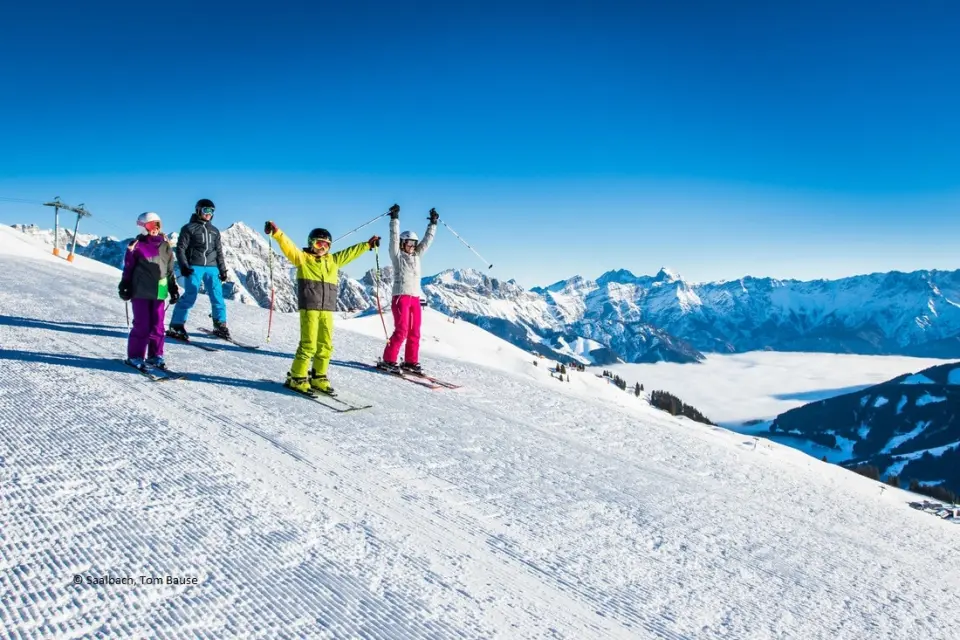 Familie beim Skifahren auf sonniger Piste mit majestätischem Bergpanorama im Skigebiet Saalbach, nahe Hotel Hasenauer.