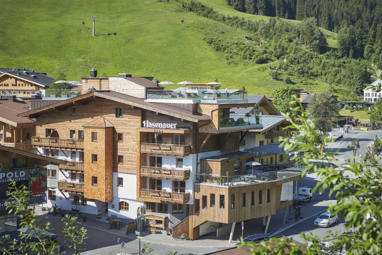 Aussenansicht des Hotel Hasenauer in den Alpen mit traditioneller Holzfassade und Dachterrasse vor grünen Berghängen.