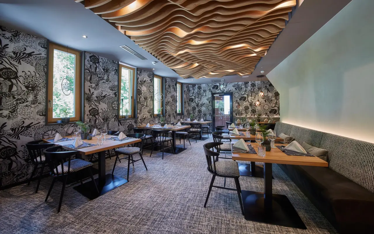 Modernes Restaurant im Hotel Hasenauer mit stilvoller Einrichtung, Holztischen und Designer-Decke.