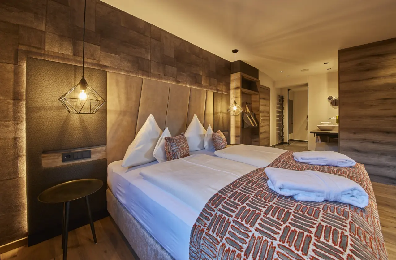 Modernes Doppelzimmer im Hotel Hasenauer mit Holzelementen, gemütlichem Bett und offenem Badbereich.