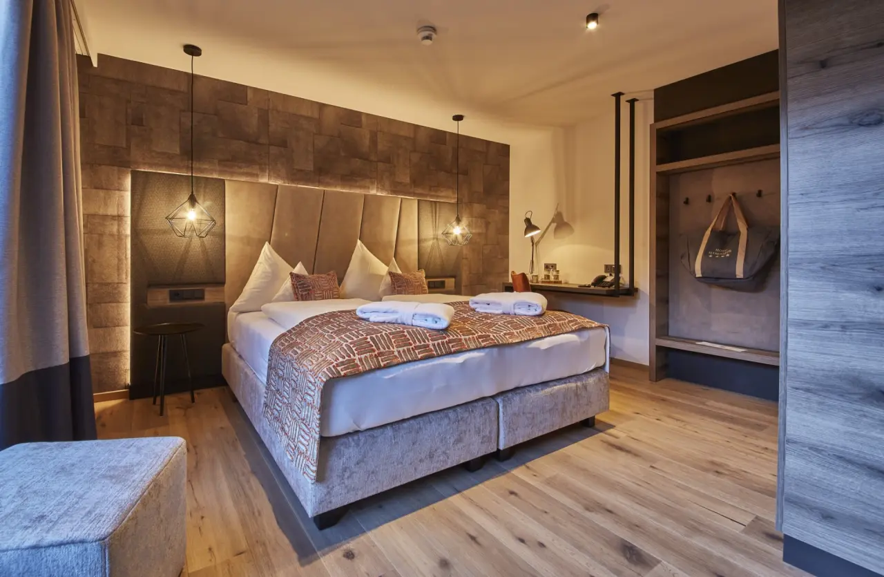 Modernes Doppelzimmer im Hotel Hasenauer mit Holzboden, gemütlichem Bett und stilvoller Beleuchtung.