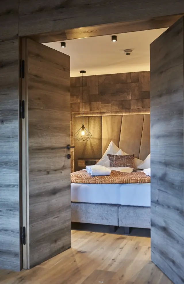 Modernes Doppelzimmer im Hotel Hasenauer mit Holzelementen, gemütlichem Bett und stilvoller Beleuchtung.