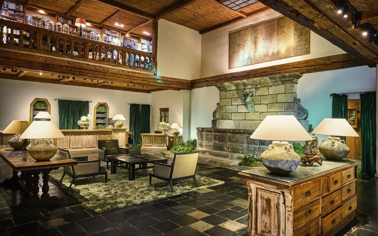 Geräumige Lobby des Bleiche Resort & Spa mit rustikalem Design, Steinbrunnen, gemütlichen Sitzbereichen und Bibliotheksempore.