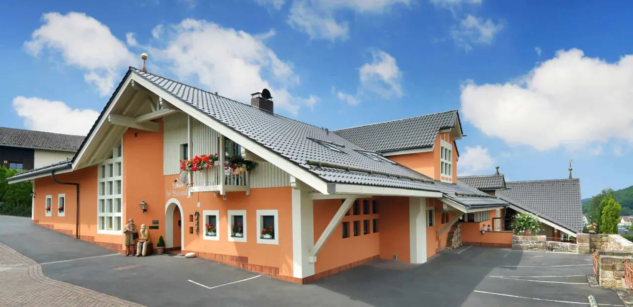Aussenansicht des Landhaushotels Hof Wasserkuppe mit oranger Fassade, Giebeldach und Blumenkästen unter blauem Himmel.
