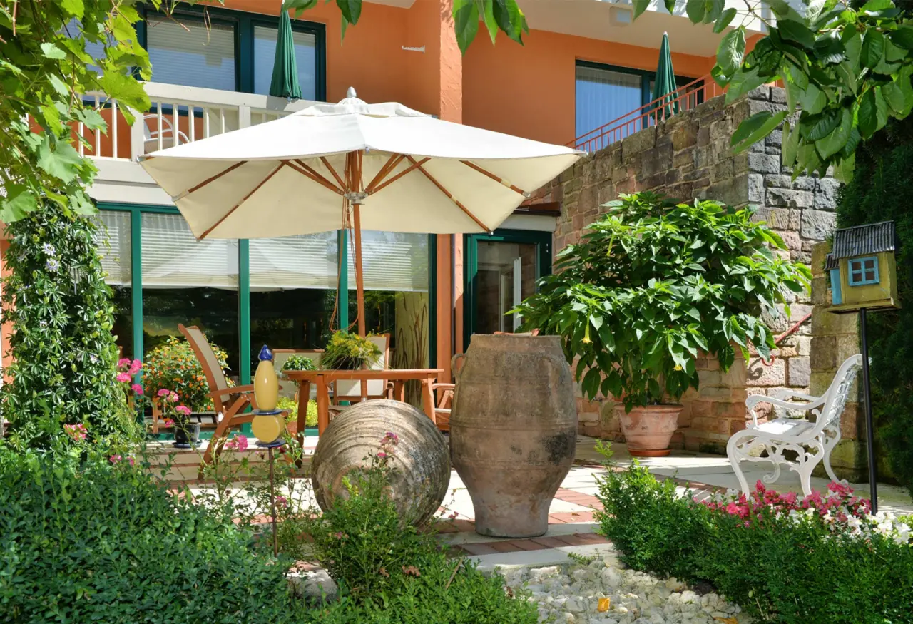 Gemütlicher Hotelgarten mit Terrasse, Sonnenschirm und Sitzgelegenheiten im Landhaushotel Hof Wasserkuppe.