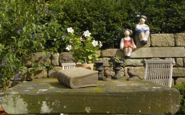 Dekorative Gartenszene mit Steintisch, Blumen und Figuren im Landhaushotel Hof Wasserkuppe.
