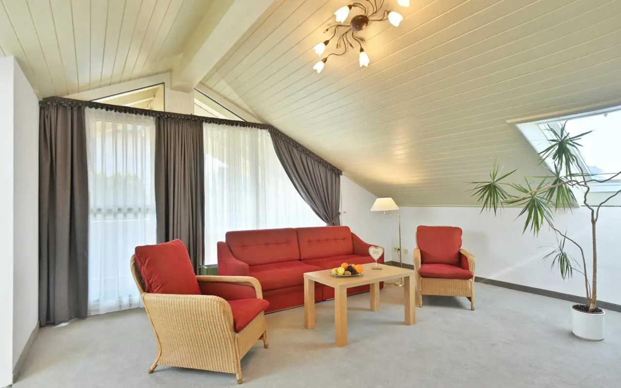 Gemütlicher Wohnbereich einer Suite mit rotem Sofa und Korbsesseln im Landhaushotel Hof Wasserkuppe.