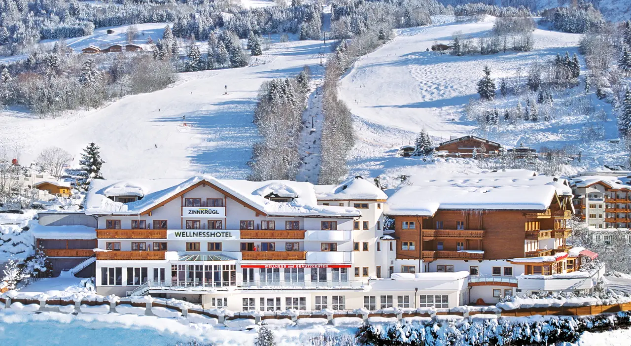 Wellness Hotel Zinnkrügl im Winter mit verschneiten Dächern und direkter Lage an der Skipiste in den Alpen.