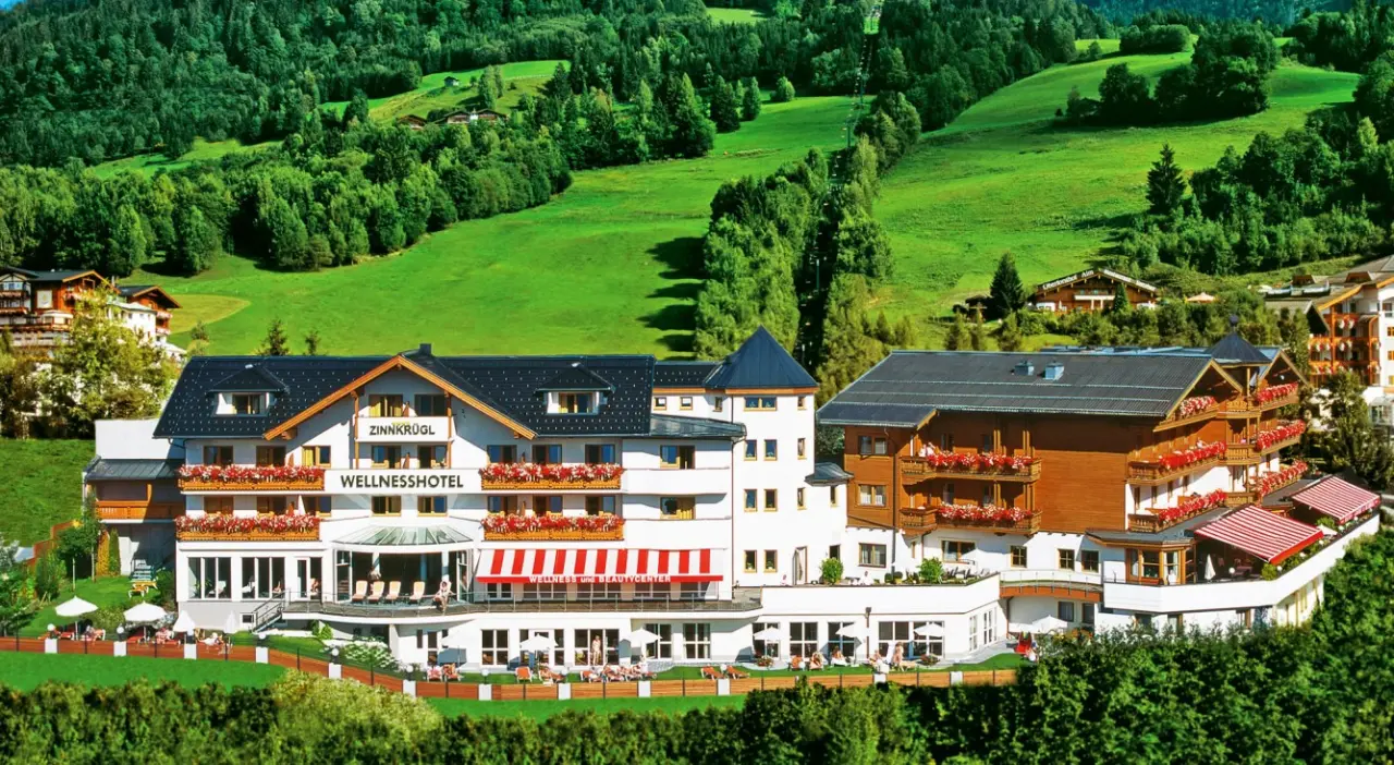 Aussenansicht des Wellness Hotel Zinnkrügl in grüner Berglandschaft mit blühenden Balkonen und Sonnenterrassen.