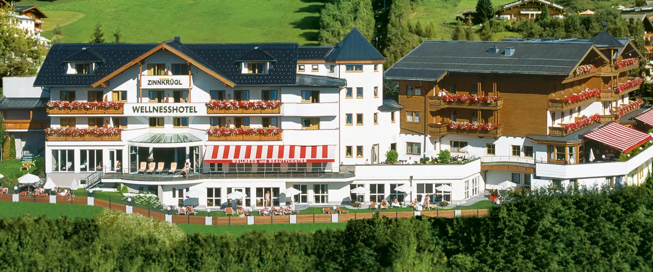 Aussenansicht des Wellness Hotel Zinnkrügl mit blühenden Balkonen und Sonnenterrasse in grüner Berglandschaft.