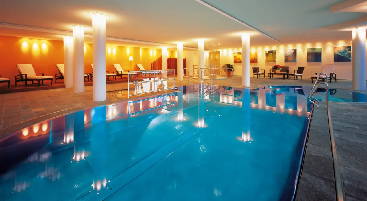 Grosszügiger Innenpoolbereich mit warmem Licht und bequemen Liegen im Wellness Hotel Zinnkrügl.