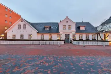 Historische Fassade des Hotel Stadt Hamburg bei Dämmerung mit beleuchteten Fenstern und weißem Zaun.