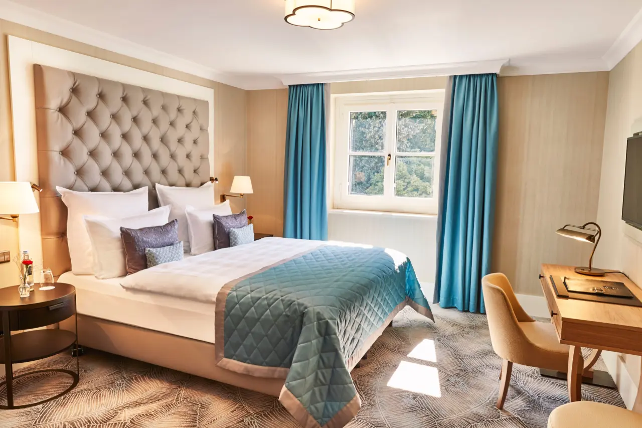 Komfortables Doppelzimmer im Steigenberger Grand Petersberg mit elegantem Bett, Schreibtisch und Blick ins Grüne.