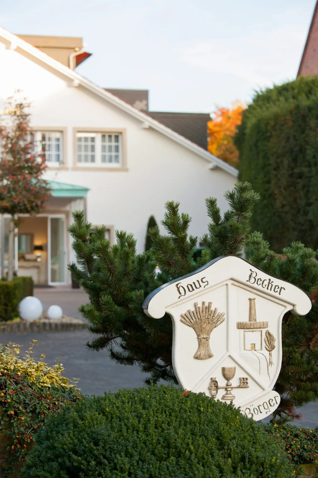 Hölzernes Wappen-Schild mit 'Haus Becker' Schriftzug und traditionellen Motiven am Eingang des Ferienhotels Haus Becker.