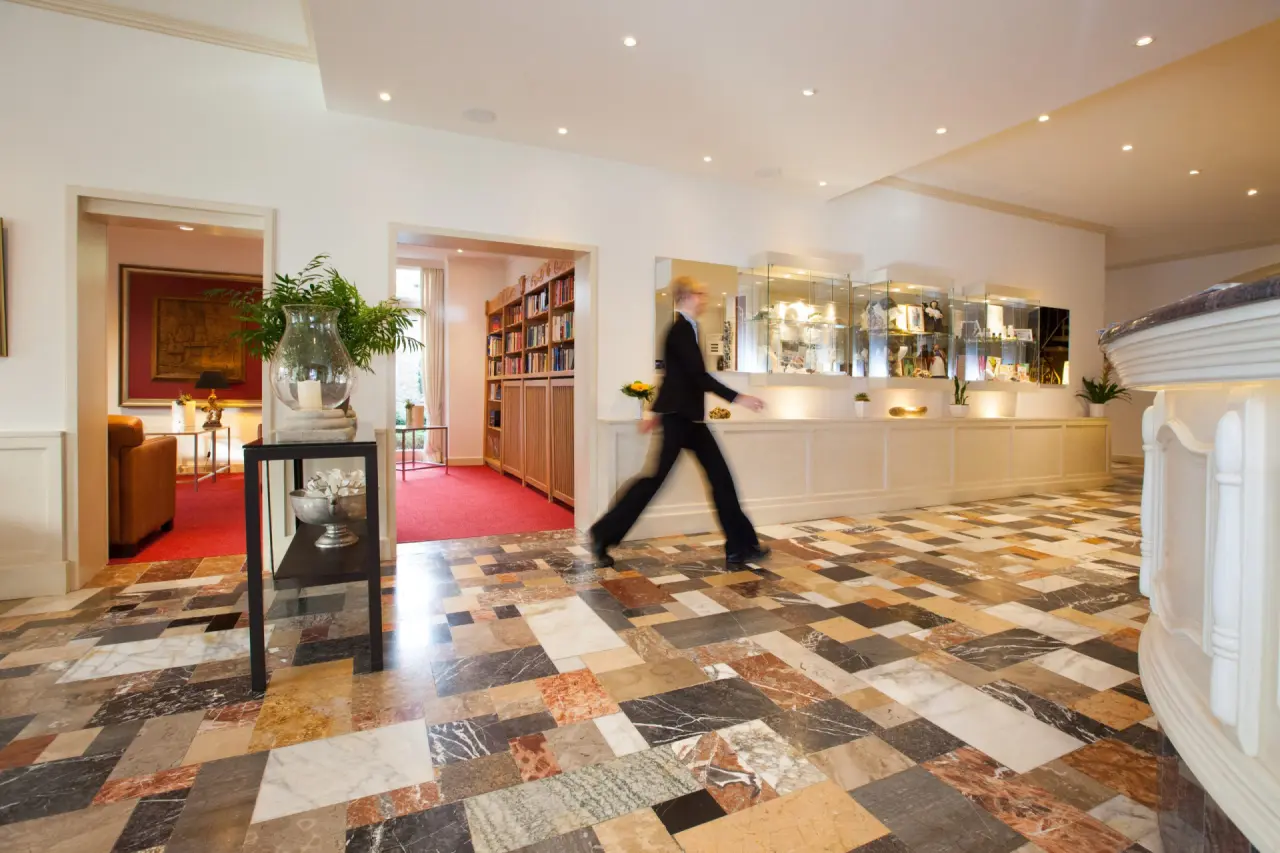 Helle Lobby des Ferienhotel Haus Becker mit gemustertem Marmorboden, Rezeption und Durchgang zu Bibliothek und Lounge.
