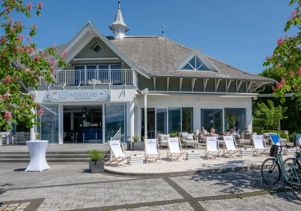 Werzers Bootshaus mit Seeterrasse und entspannten Gästen unter blauem Himmel im Werzers Hotel Resort Pörtschach.