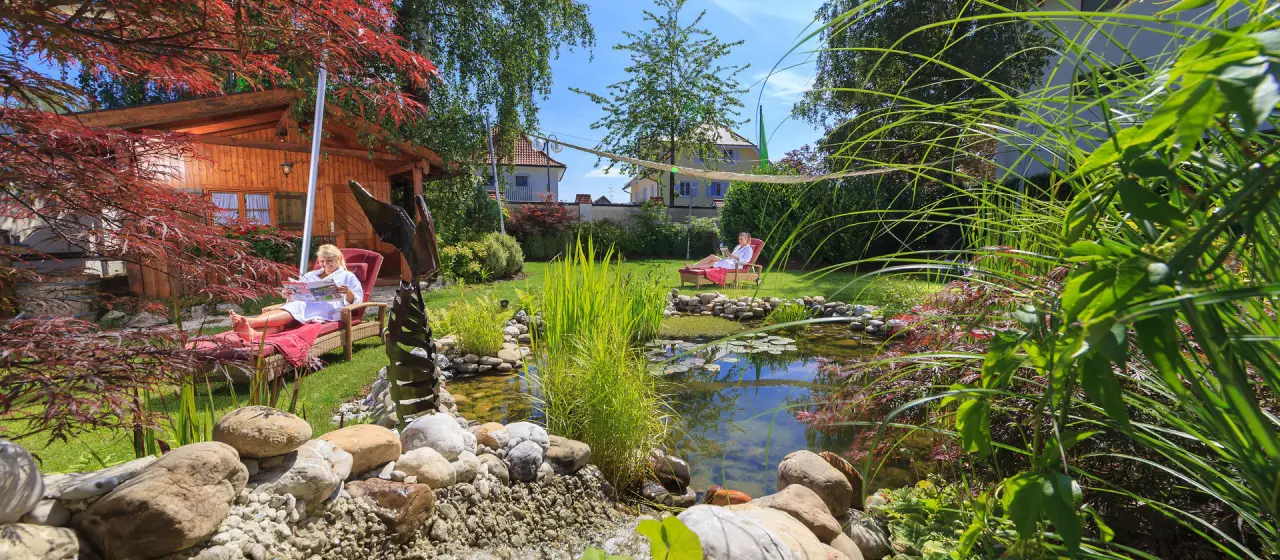 Idyllischer Hotelgarten mit Naturteich, Bachlauf und entspannenden Liegen im Kneipp- & Wellvitalhotel Edelweiss.