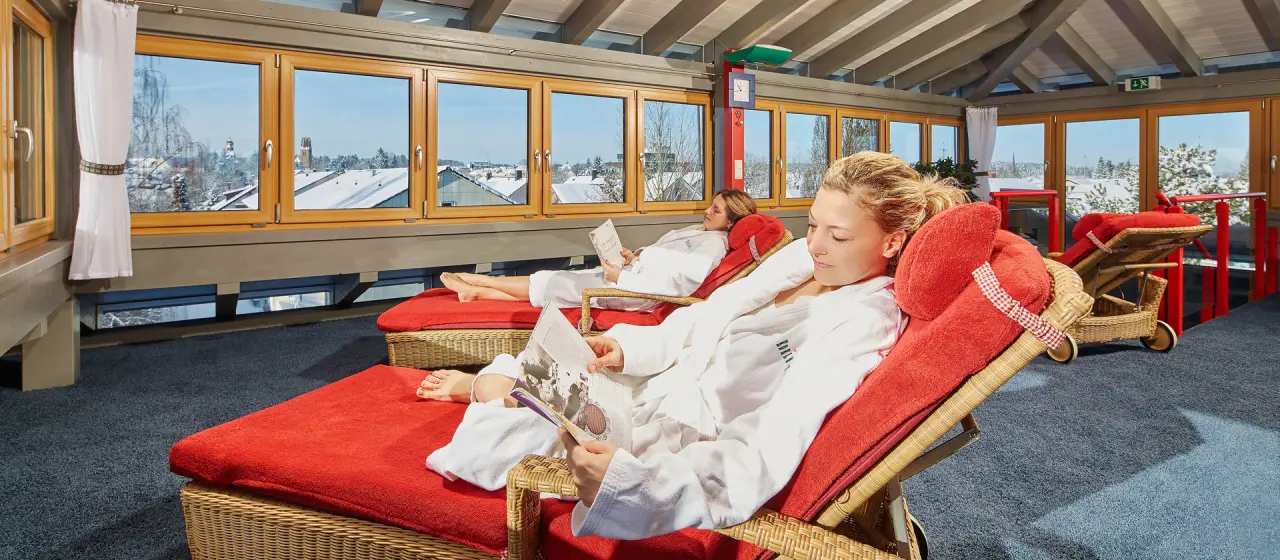 Gäste entspannen in Liegestühlen im Ruheraum mit Winterpanorama im Kneipp- & Wellvitalhotel Edelweiss.