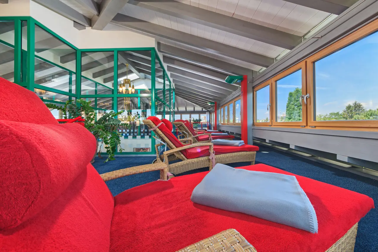 Entspannungsbereich mit roten Liegen und grossen Fenstern im Kneipp- & Wellvitalhotel Edelweiss.