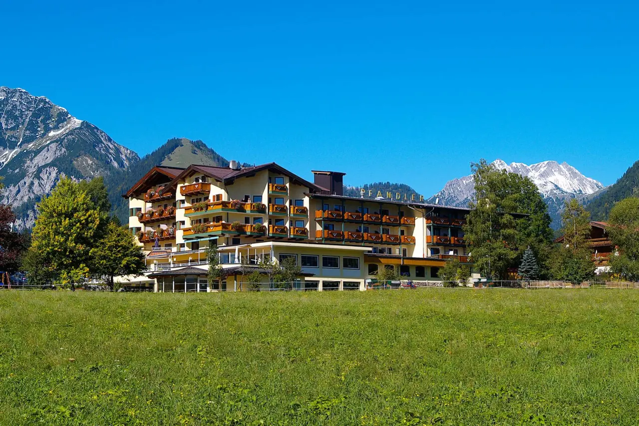 Das Pfandler Hotel in den Tiroler Alpen, umgeben von grünen Wiesen und majestätischen Bergen unter strahlend blauem Himmel.