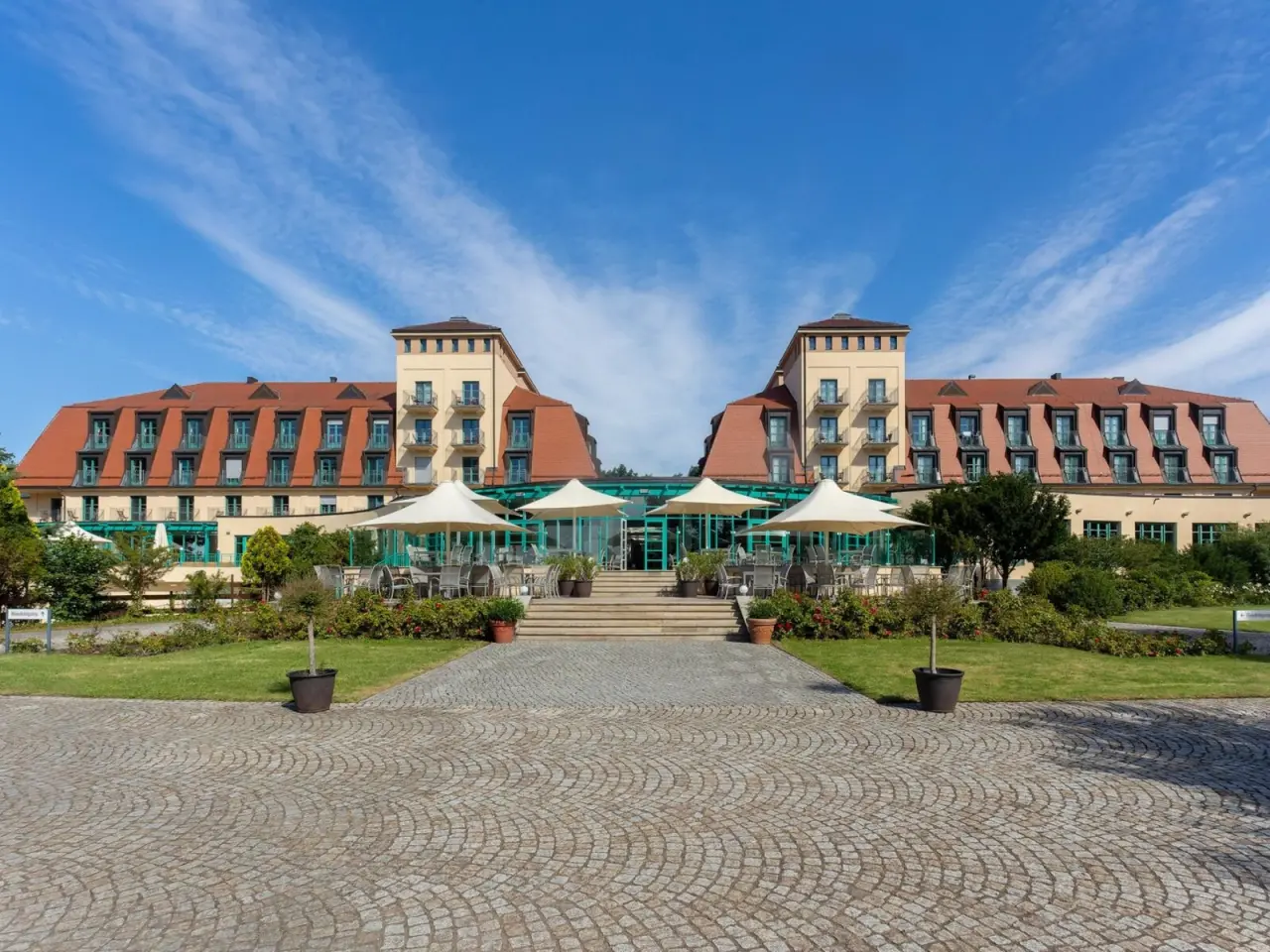 Aussenansicht des Precise Resort Bad Saarow mit Terrasse und Garten unter blauem Himmel.