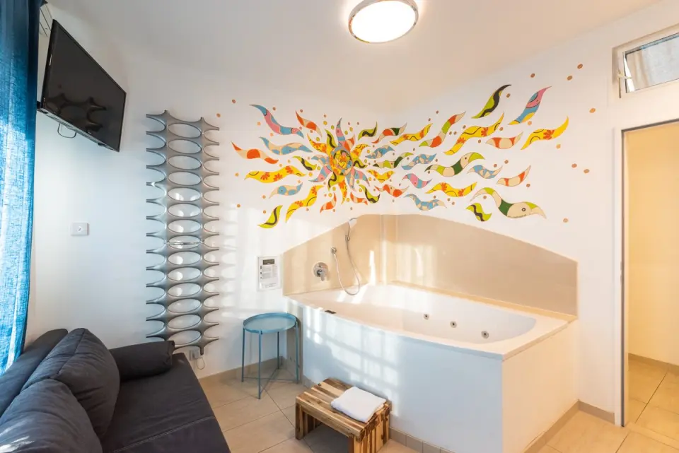 Jacuzzi Badewanne mit bunter Wandmalerei und Sofa in einem Zimmer im Wellnesshotel Ziegelruh.