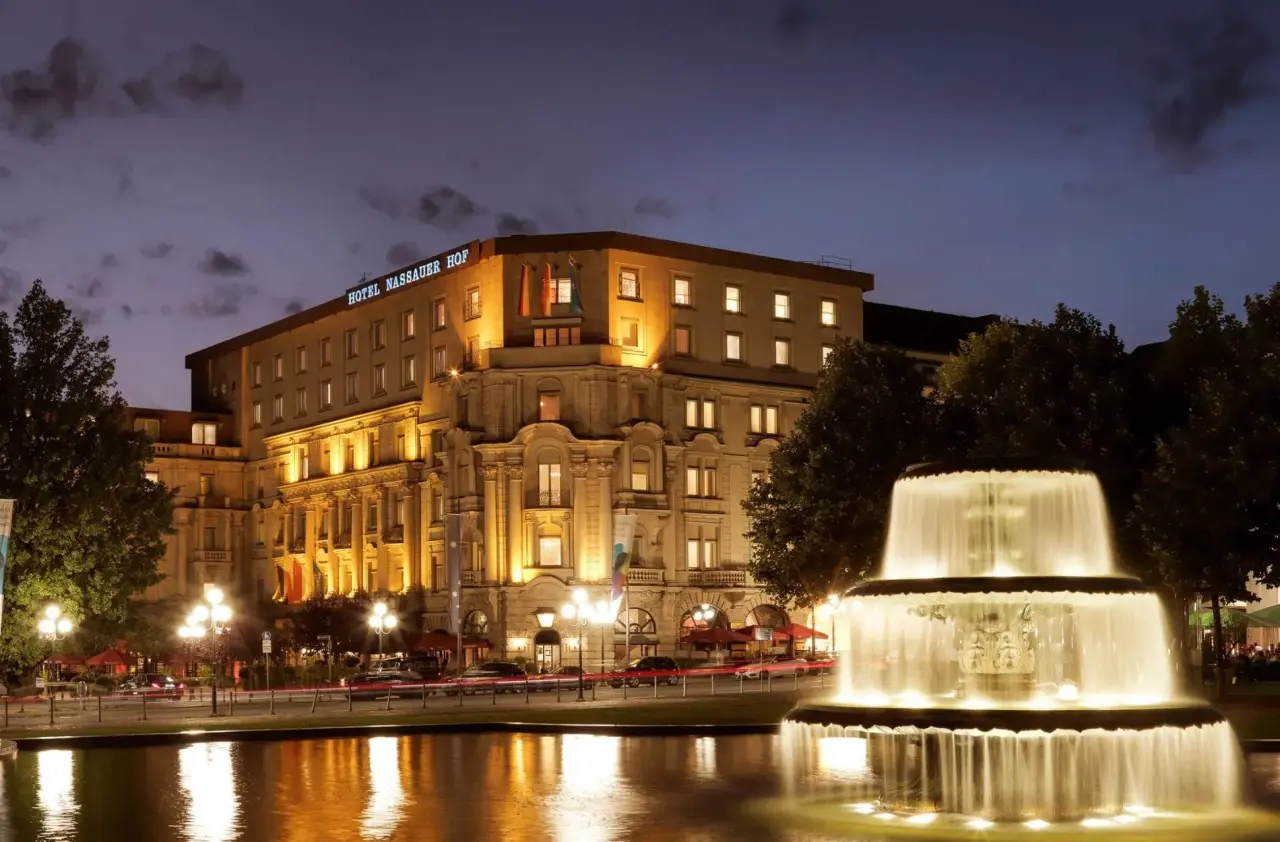 Beleuchtete Fassade des Luxushotels Nassauer Hof bei Nacht mit einem hell erleuchteten Brunnen im Vordergrund.