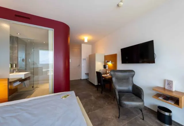 Modernes Hotelzimmer im AVIVA****s make friends mit Doppelbett, Schreibtisch und offenem Badbereich.