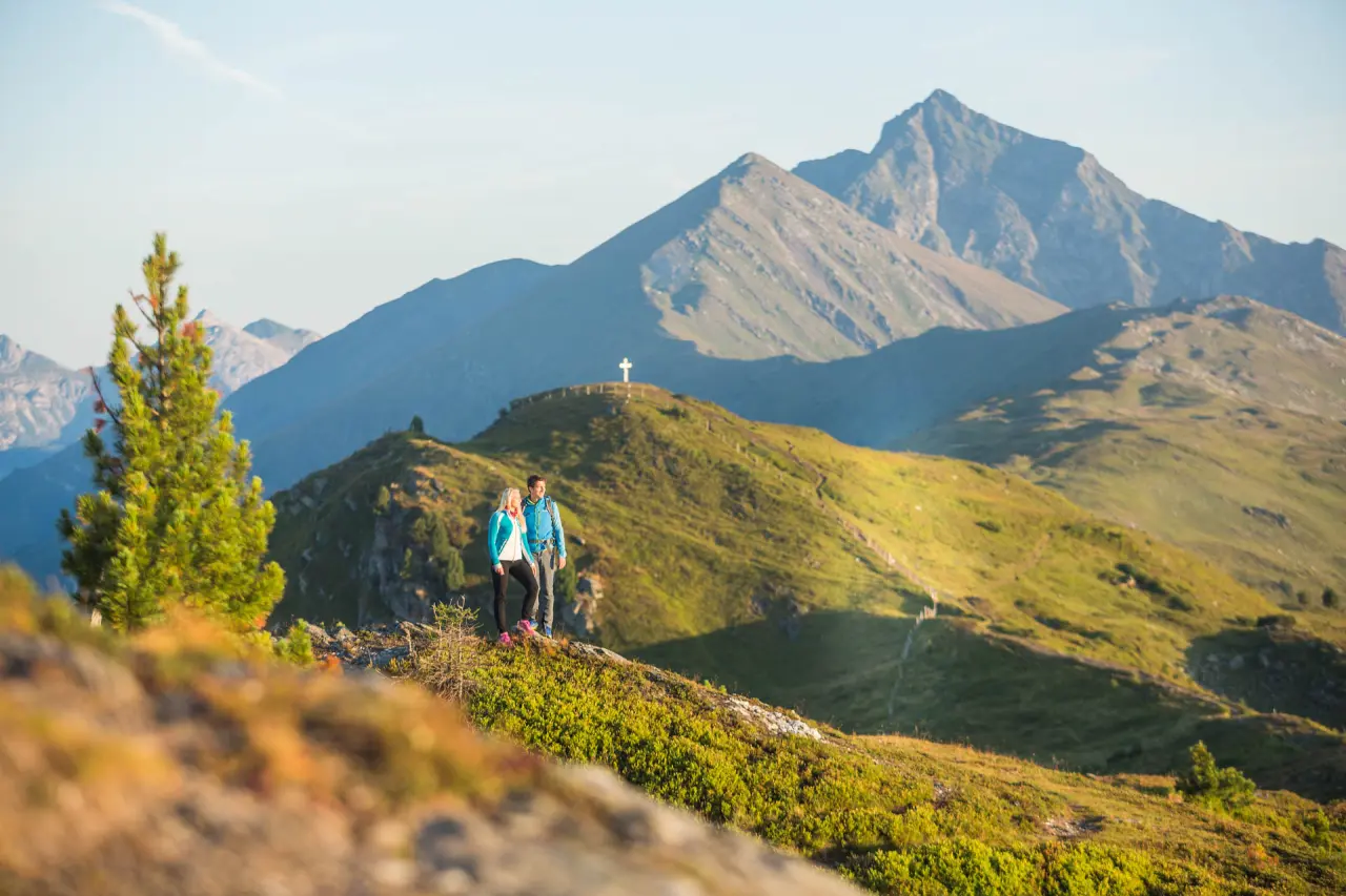 Wandererpaar genießt die Berglandschaft mit Gipfelkreuz in den Alpen nahe dem Romantik Hotel Wastlwirt.