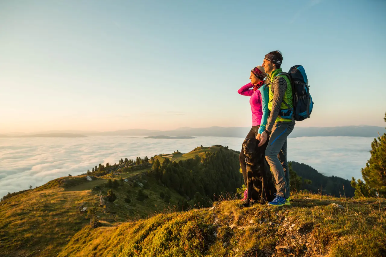 Wanderer mit Hund genießen den Sonnenaufgang über dem Wolkenmeer in den Bergen nahe dem Romantik Hotel Wastlwirt.