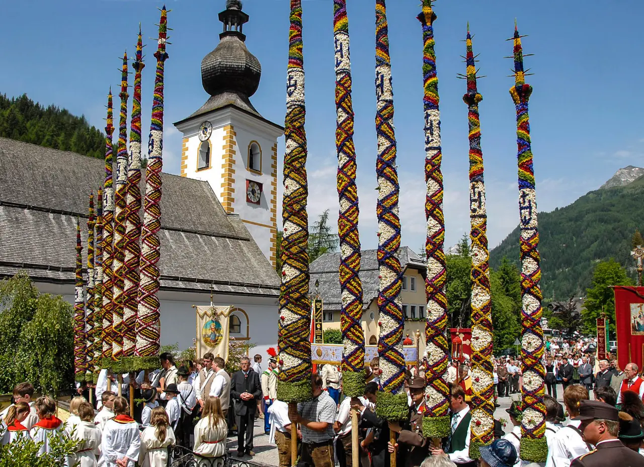 Traditionelle Prozession mit farbenfrohen Blumenstangen und Kirche im Bergdorf, nahe Romantik Hotel Wastlwirt.