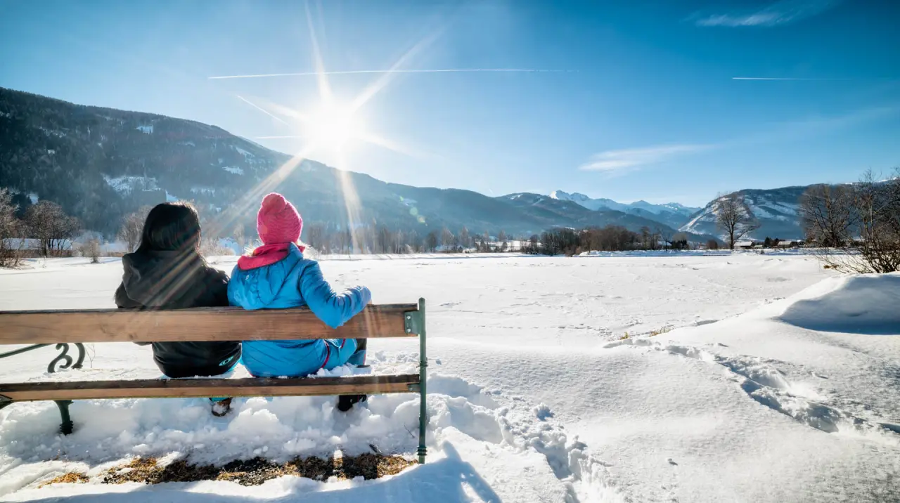 Zwei Personen auf einer Bank genießen die verschneite Winterlandschaft mit Bergpanorama nahe dem Romantik Hotel Wastlwirt.